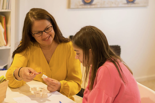 Sim guiding a child through letter blocks in a session