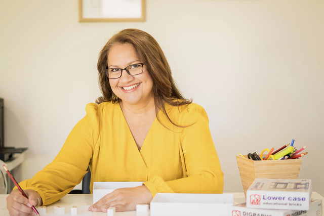 Sim smiling at her desk with educational letter bricks
